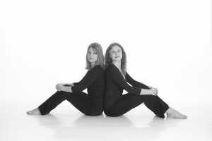 Atomic Partnership Ltd. Two women sitting back to back and looking toward the camera.